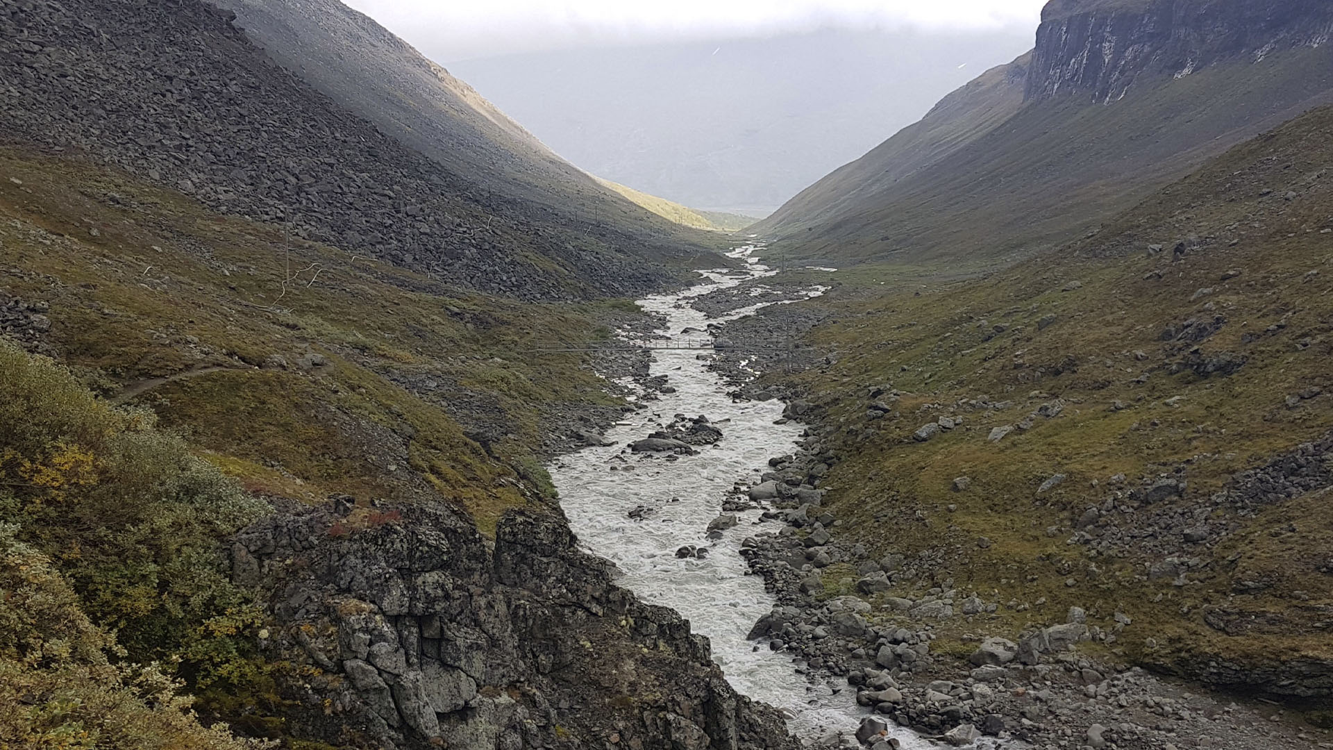 Vattendrag rinner mellan fjälltoppar.