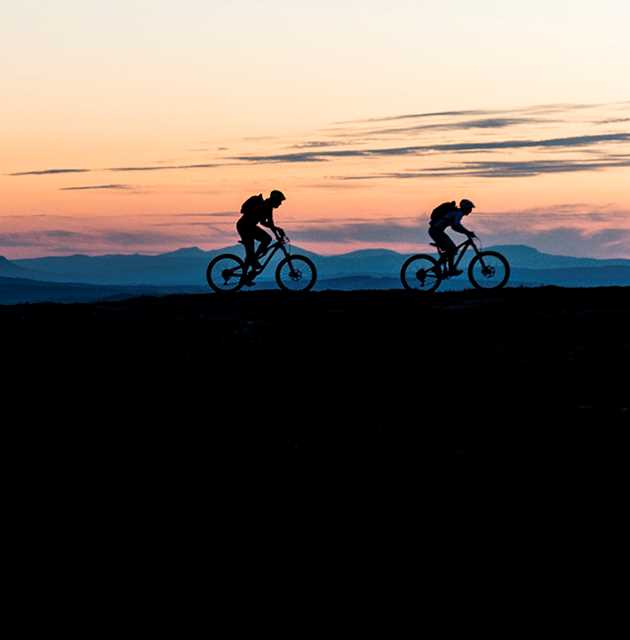 Två mountainbikecyklister syns i siluett mot en kvällshimmel